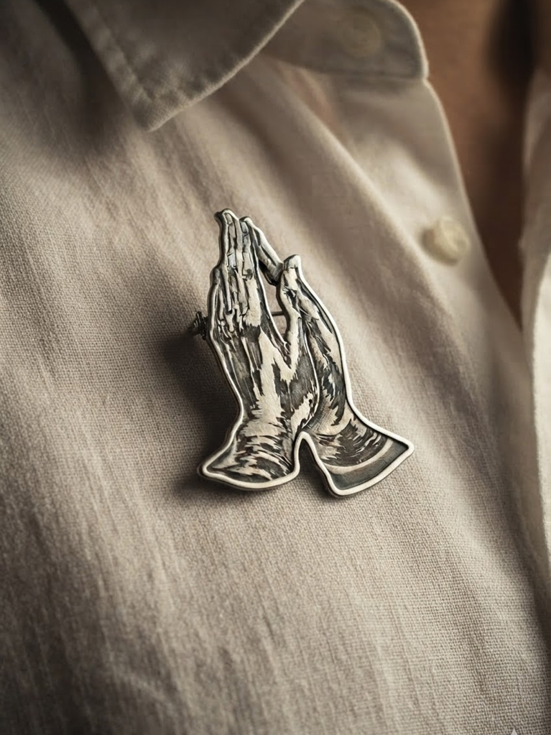 Rebus enamel pin shaped like praying hands, pinned to fabric